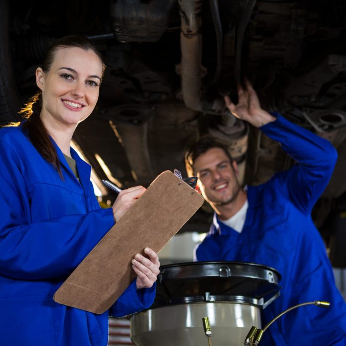 Mechanics preparing a check list while his colleague examining a car engine in the background